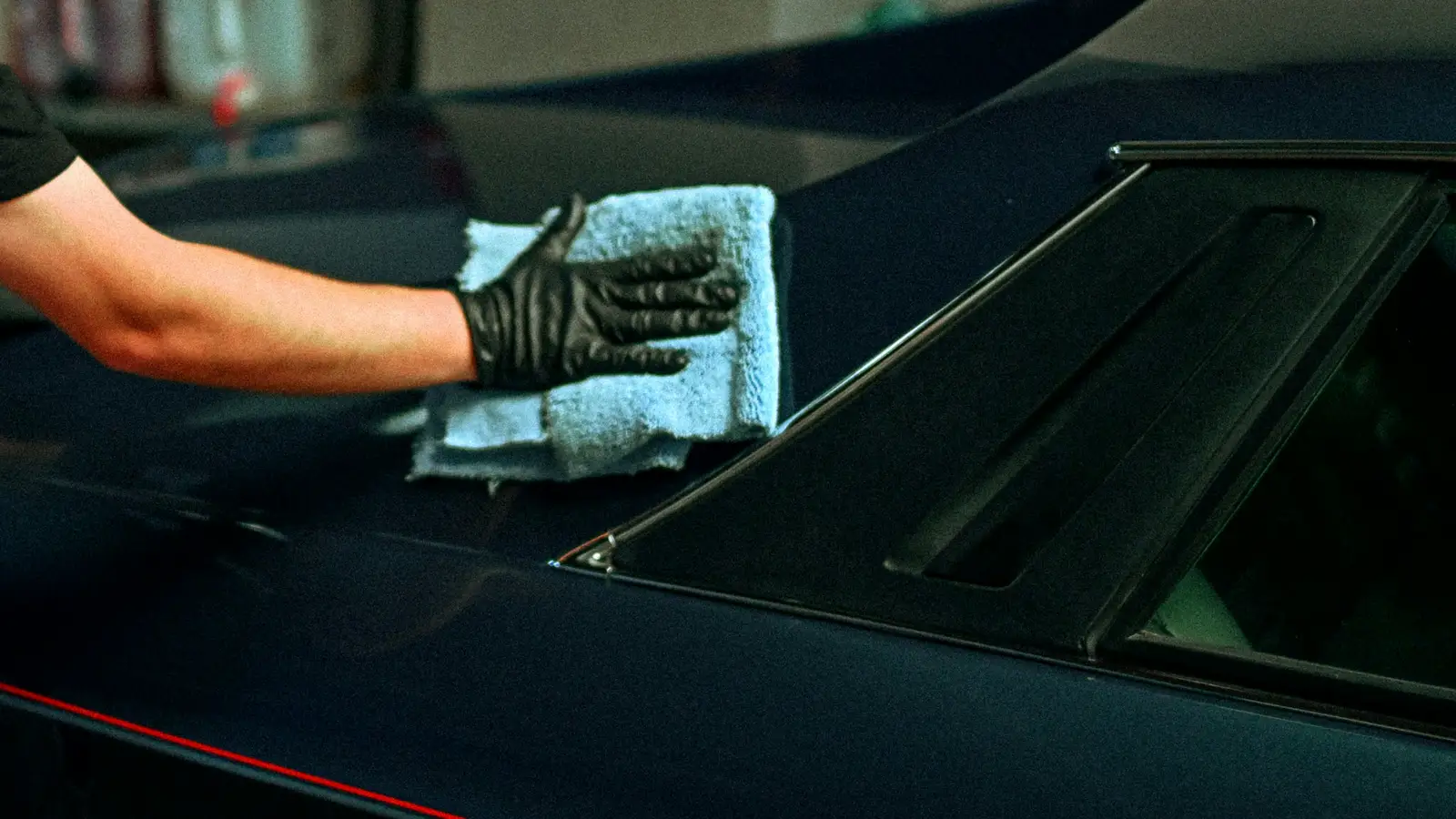 A gloved hand wiping a dark blue car panel with a microfiber towel